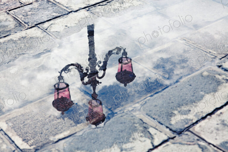 The reflection of an ornate street lamp in a puddle on a rainy day in Venice, Italy.