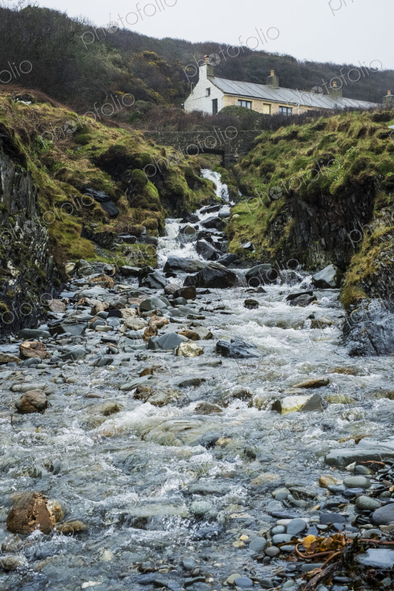 The rocky shore of Pembrokeshire, a bay with a cottage by the water and steps to the…