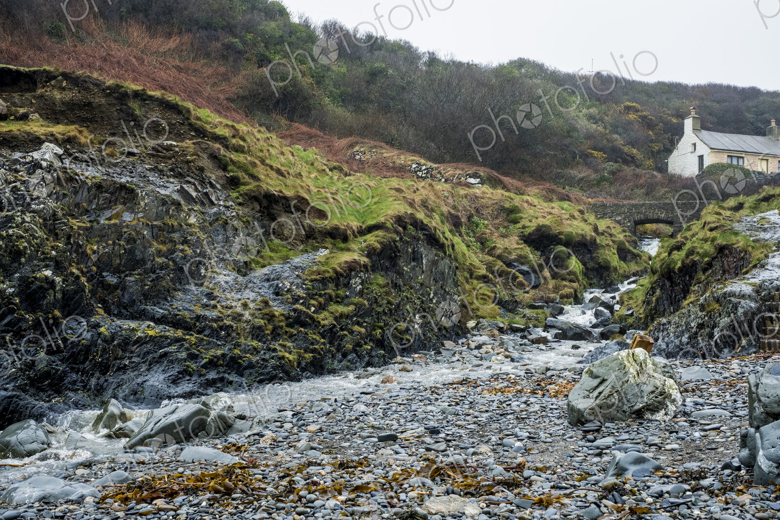 The rocky shore of Pembrokeshire, a bay with a cottage by the water and steps to the…