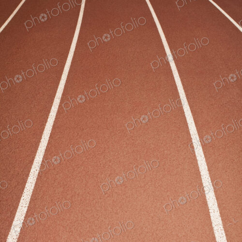 The surface of a sports athletics running track, red surface with white painted lane…