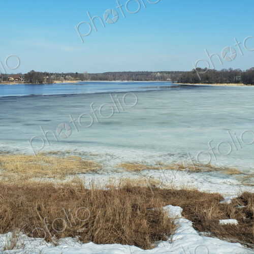The view across a river in winter, with ice on the surface.