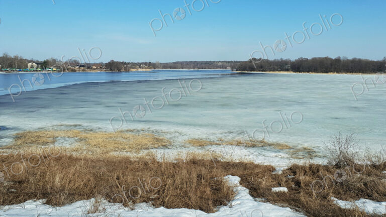 The view across a river in winter, with ice on the surface.