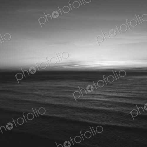 The water surface of the ocean at dusk, black and white, ripples and waves.