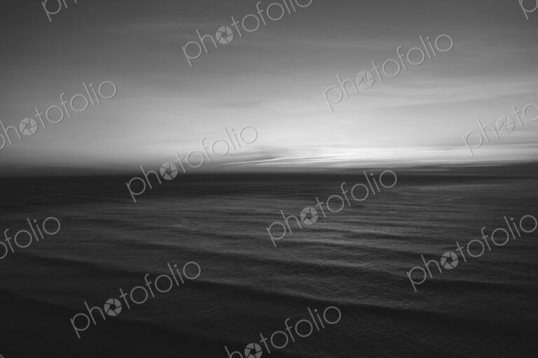 The water surface of the ocean at dusk, black and white, ripples and waves.