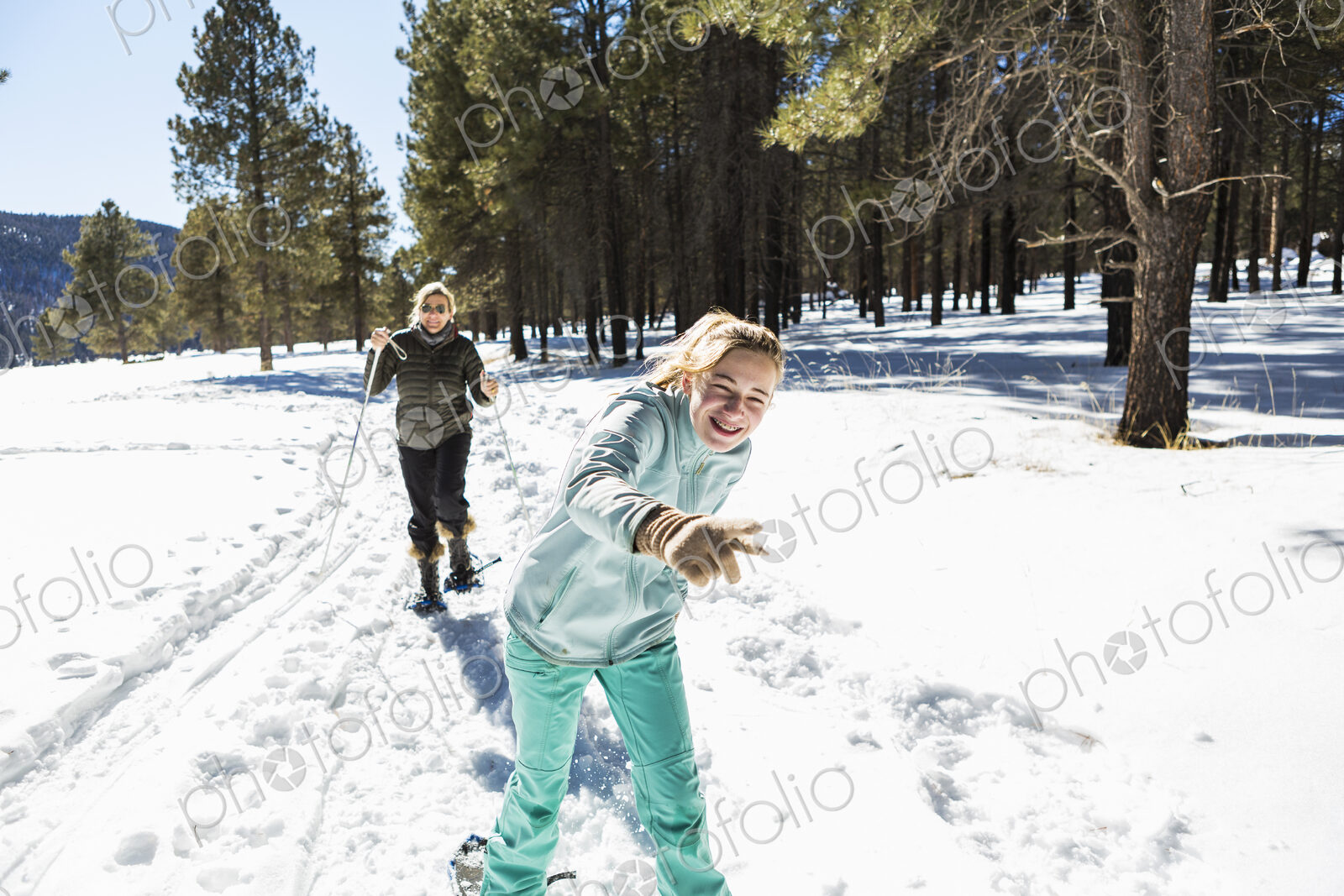 Thirteen year old girl and her mother on snow shoes on a trail in snow.
