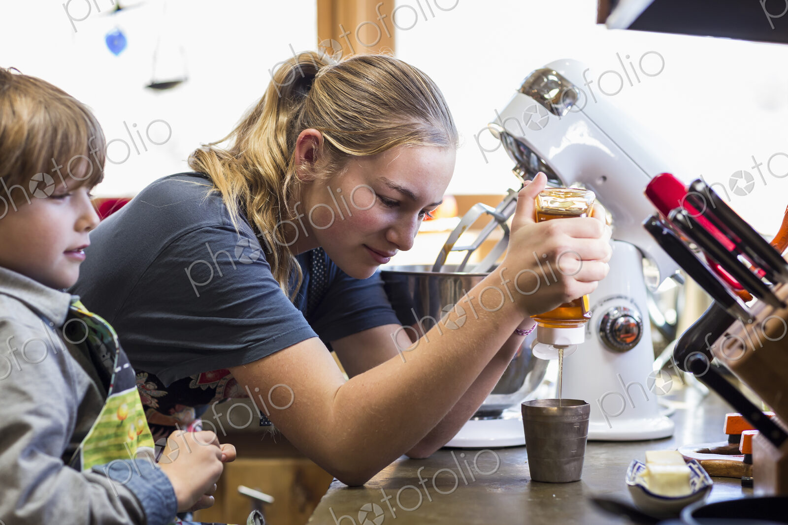 Thirteen year old teenage girl and her 6 year od brother in the kitchen,sweezing honey…