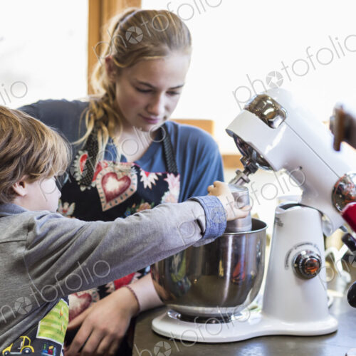 Thirteen year old teenage girl and her 6 year od brother in the kitchen,using a mixing…