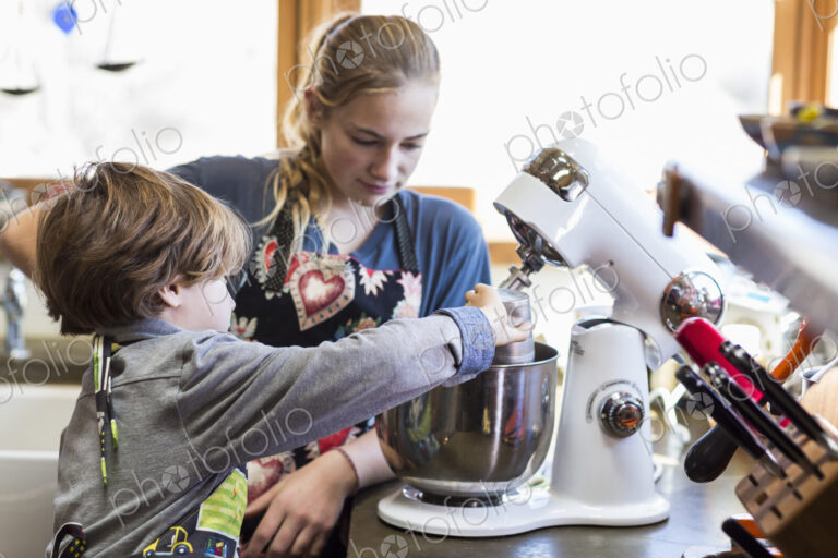 Thirteen year old teenage girl and her 6 year od brother in the kitchen,using a mixing…