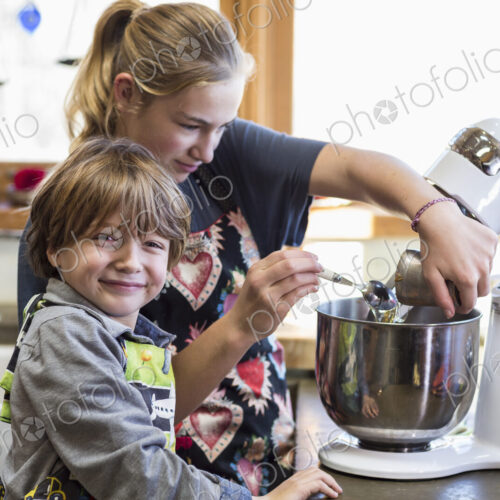 Thirteen year old teenage girl and her 6 year od brother in the kitchen,using a mixing…