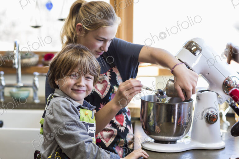 Thirteen year old teenage girl and her 6 year od brother in the kitchen,using a mixing…