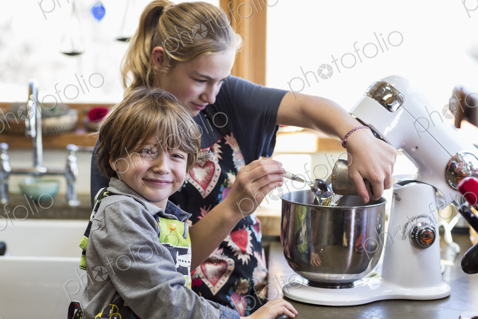 Thirteen year old teenage girl and her 6 year od brother in the kitchen,using a mixing…