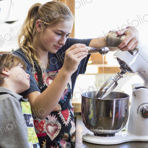 Thirteen year old teenage girl and her 6 year od brother in the kitchen,using a mixing…