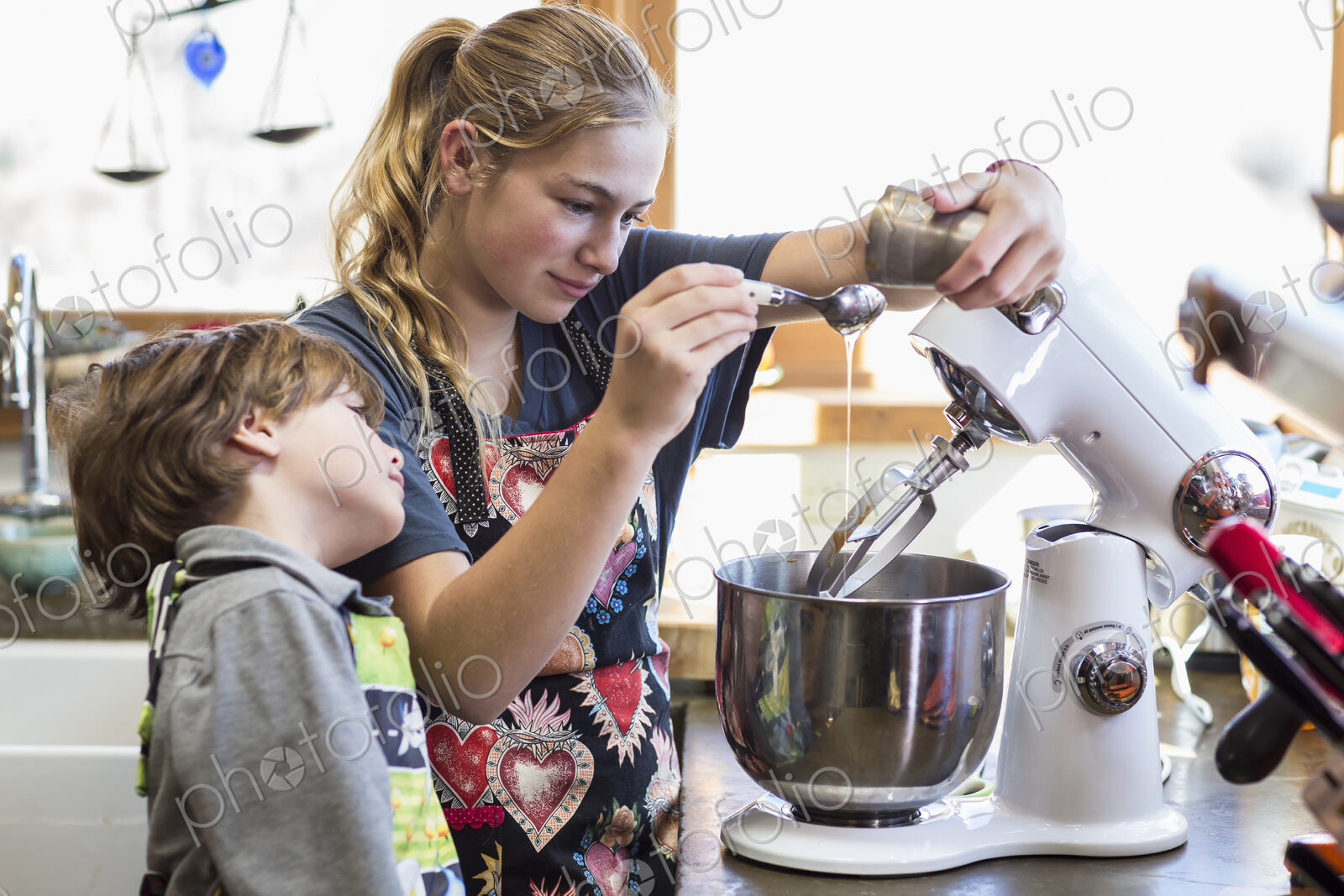 Thirteen year old teenage girl and her 6 year od brother in the kitchen,using a mixing…