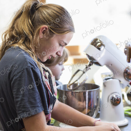 Thirteen year old teenage girl and her 6 year od brother in the kitchen,using a mixing…