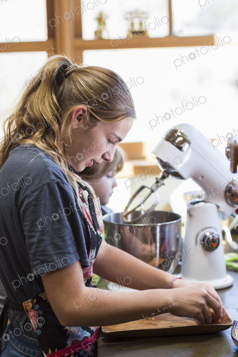 Thirteen year old teenage girl and her 6 year od brother in the kitchen,using a mixing…