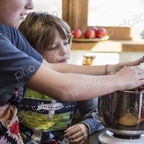 Thirteen year old teenage girl and her 6 year od brother in the kitchen,using a mixing…