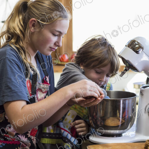 Thirteen year old teenage girl and her 6 year od brother in the kitchen,using a mixing…