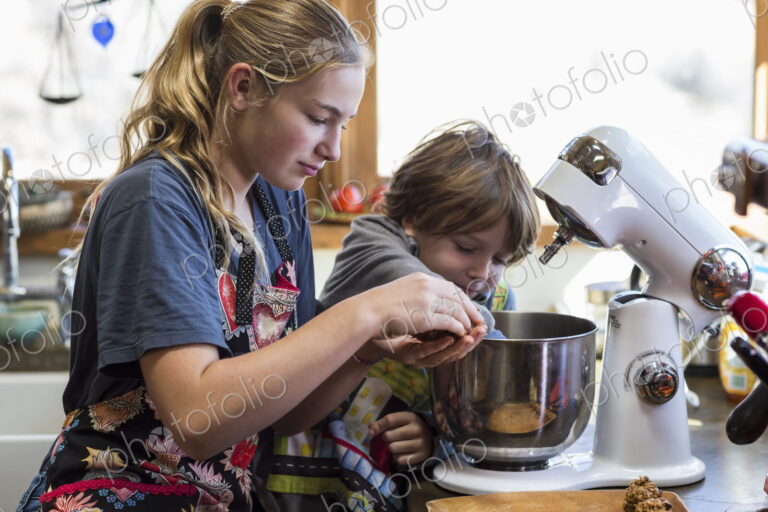 Thirteen year old teenage girl and her 6 year od brother in the kitchen,using a mixing…