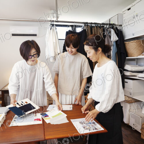 Three Japanese women standing at a table in a small fashion boutique, looking at…
