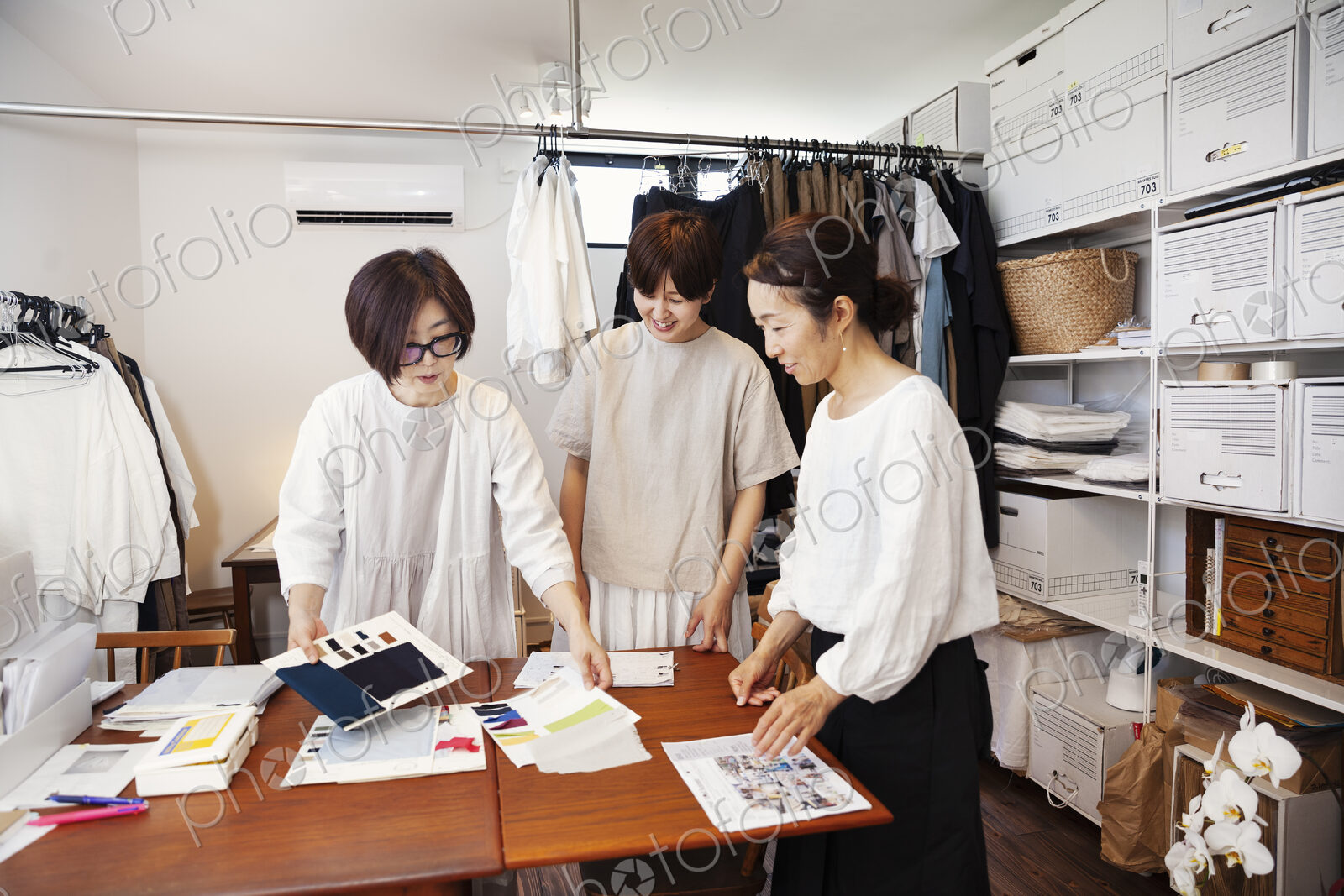 Three Japanese women standing at a table in a small fashion boutique, looking at…