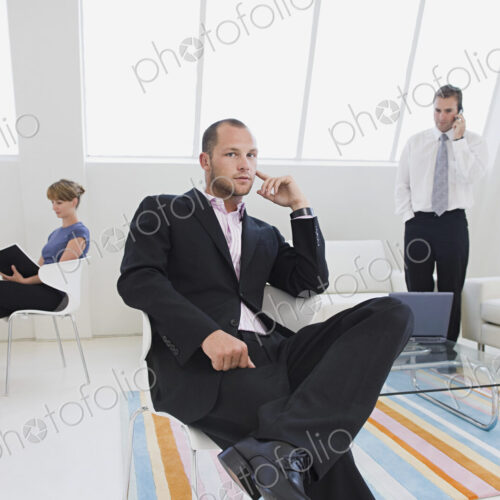 Three business people in an office, one on the phone, one working on a digital table,…