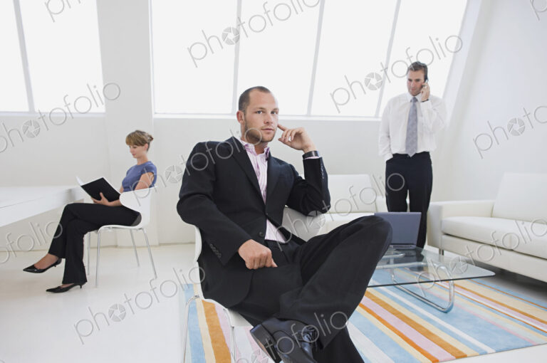 Three business people in an office, one on the phone, one working on a digital table,…