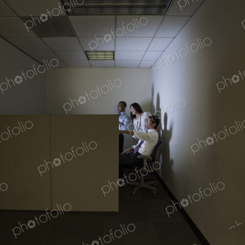 Three business people lit up by a desktop computer screen in a small corner Three business people lit up by a desktop computer screen in a small corner