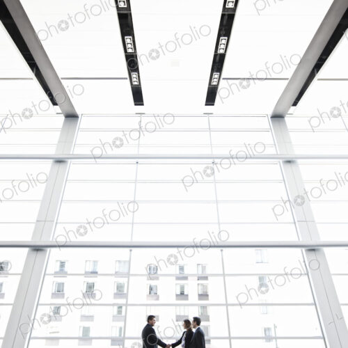 Three business people meeting in front of a large window in a conventnion center lobby. Three business people meeting in front of a large window in a conventnion center lobby.