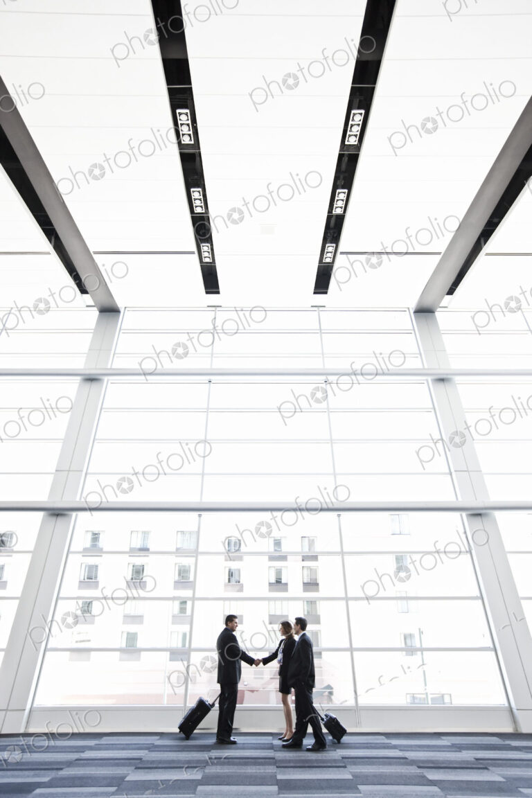 Three business people meeting in front of a large window in a conventnion center lobby.