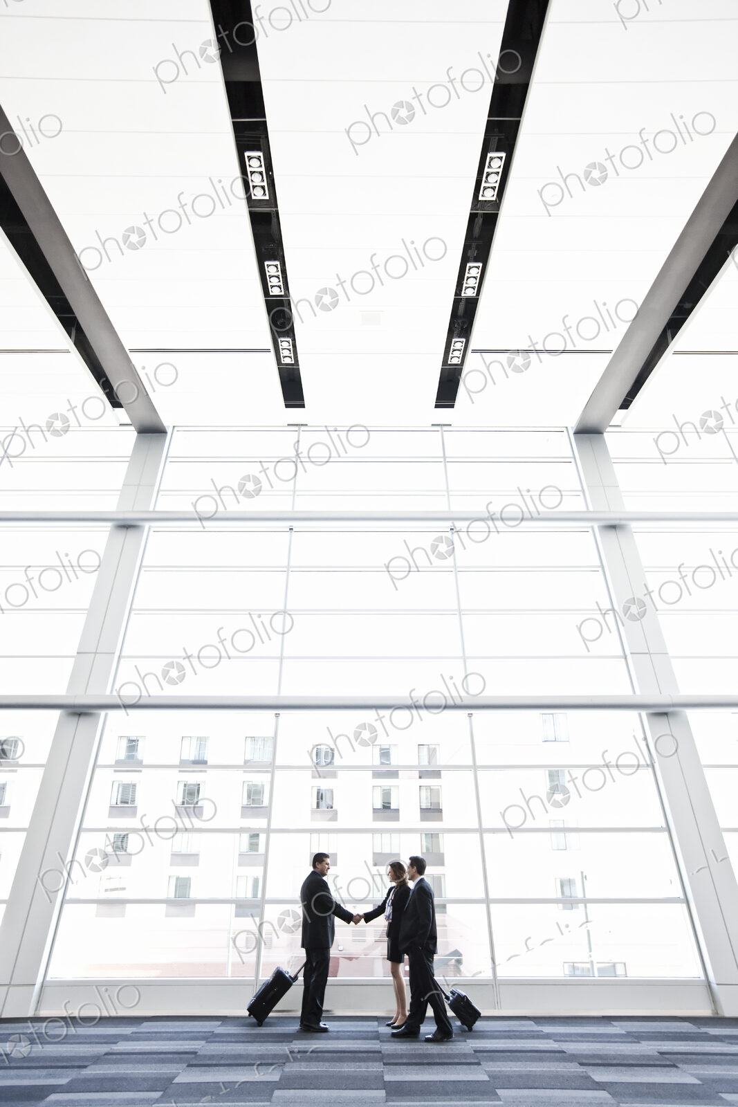 Three business people meeting in front of a large window in a conventnion center lobby.