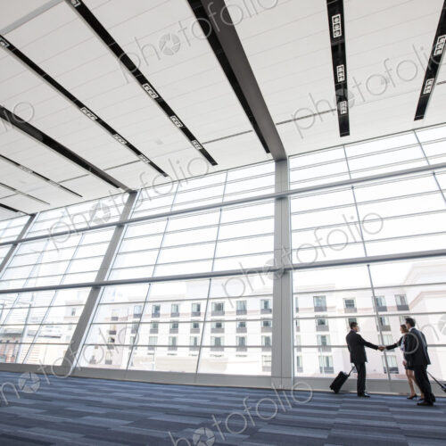 Three business people meeting in front of a large window in a conventnion center lobby. Three business people meeting in front of a large window in a conventnion center lobby.