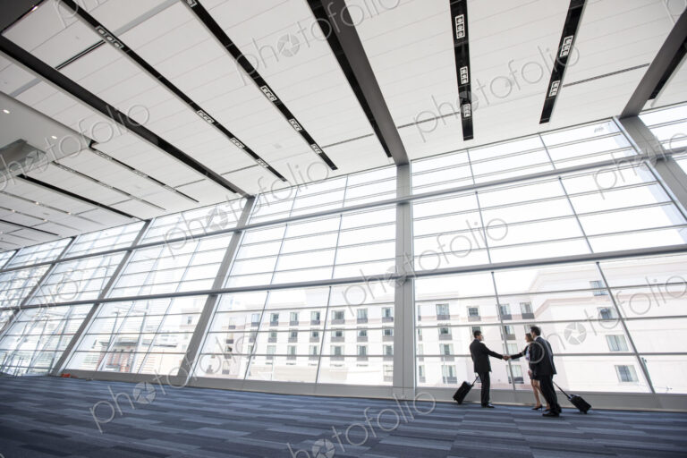 Three business people meeting in front of a large window in a conventnion center lobby.