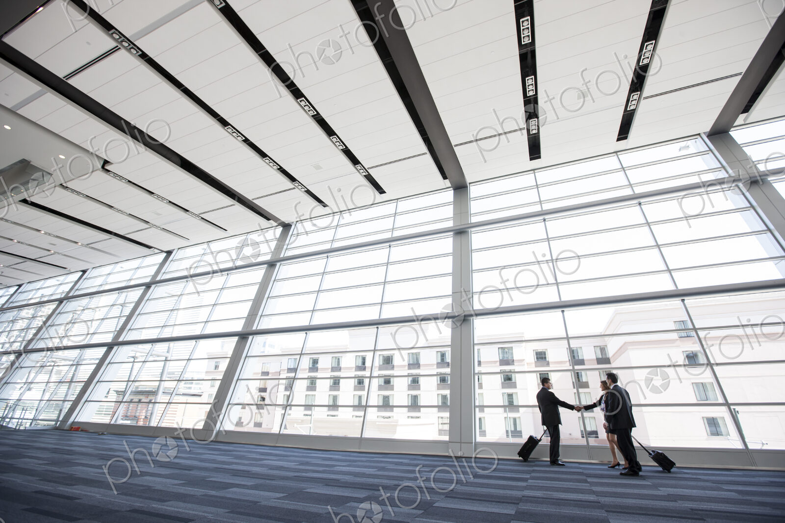 Three business people meeting in front of a large window in a conventnion center lobby.