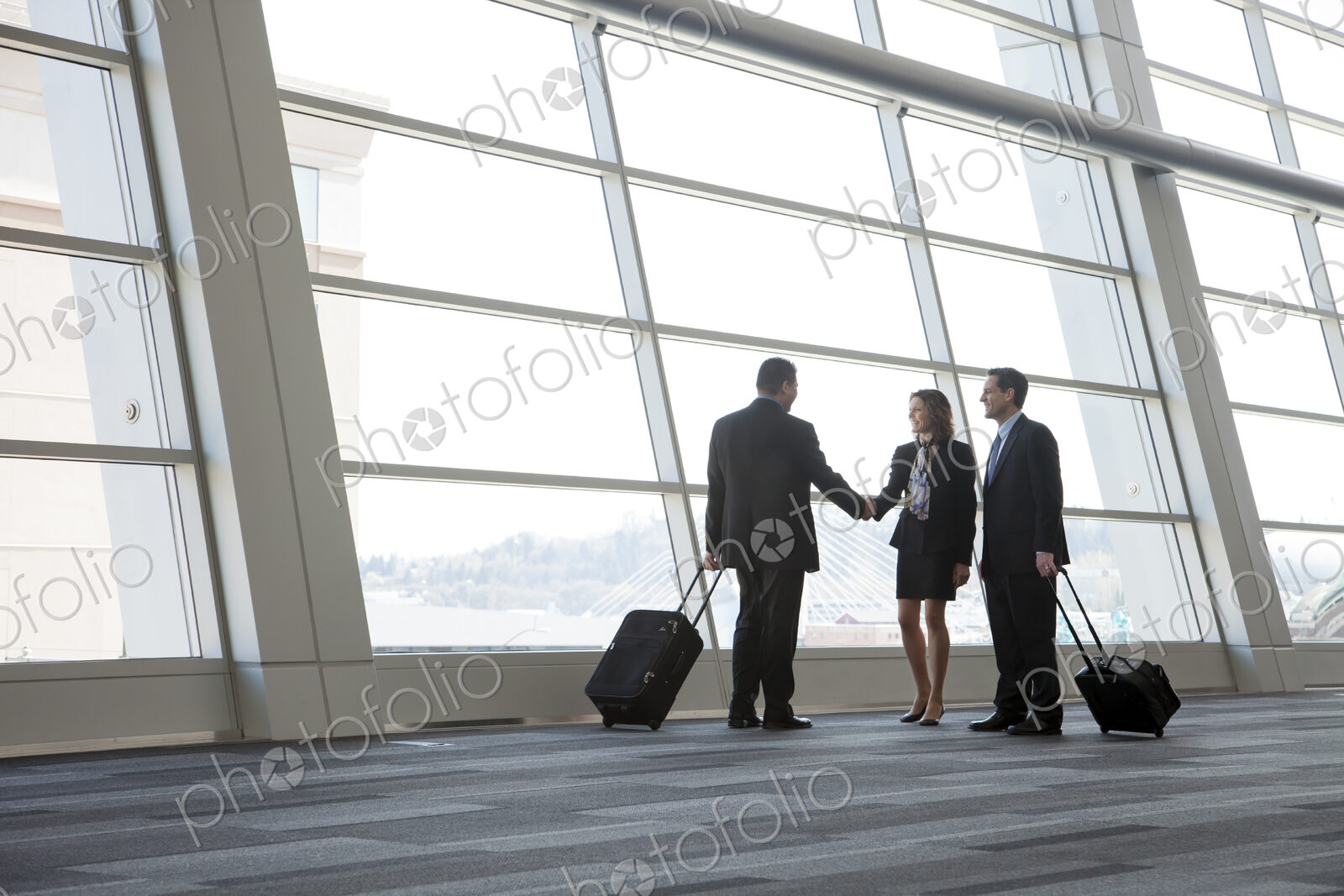Three business people meeting in front of a large window in a conventnion center lobby.