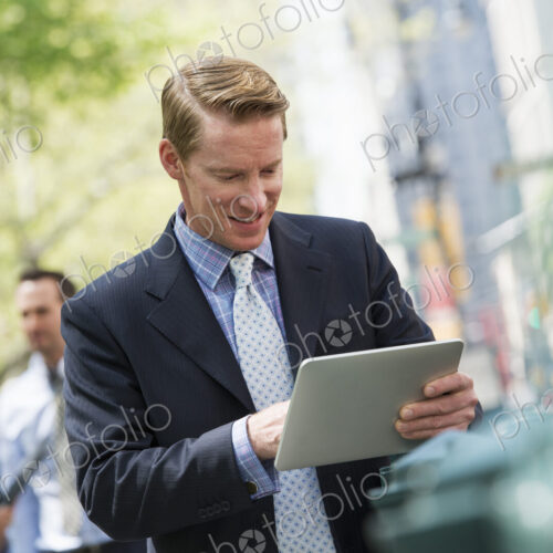 Three business people outdoors in the city. A man using a digital tablet, and a couple… Three business people outdoors in the city. A man using a digital tablet, and a couple…