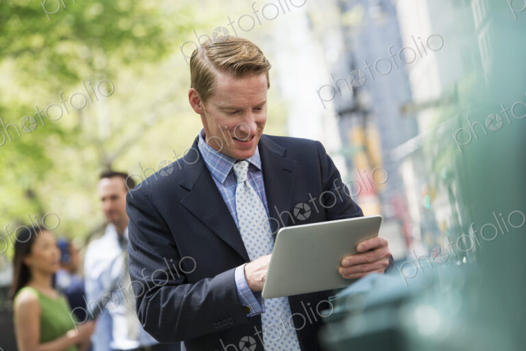 Three business people outdoors in the city. A man using a digital tablet, and a couple…