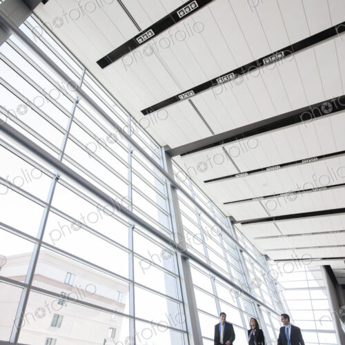 Three business people walking next to a large window in a conference centre lobby.
