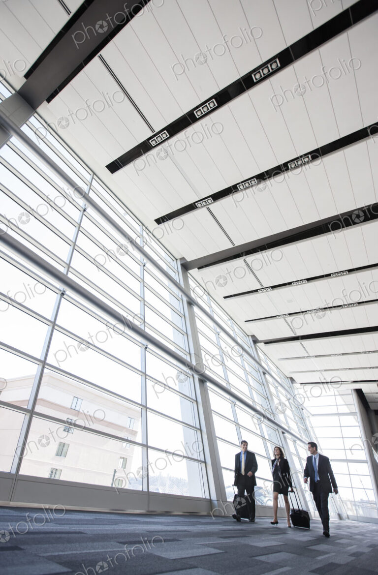 Three business people walking next to a large window in a conference centre lobby.