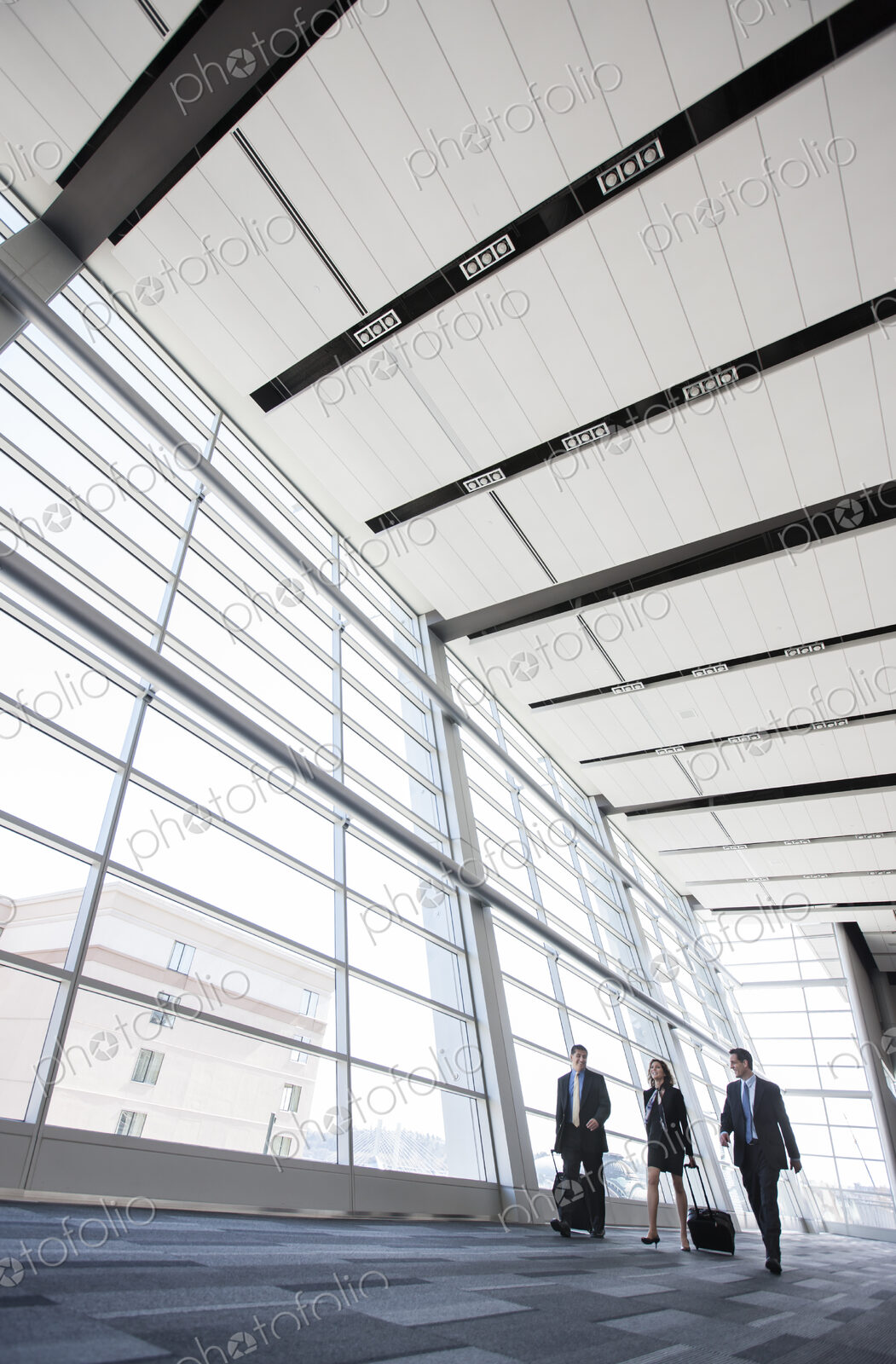 Three business people walking next to a large window in a conference centre lobby.