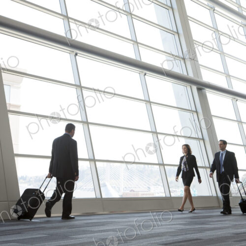 Three business people walking next to a large window in a conference centre lobby.
