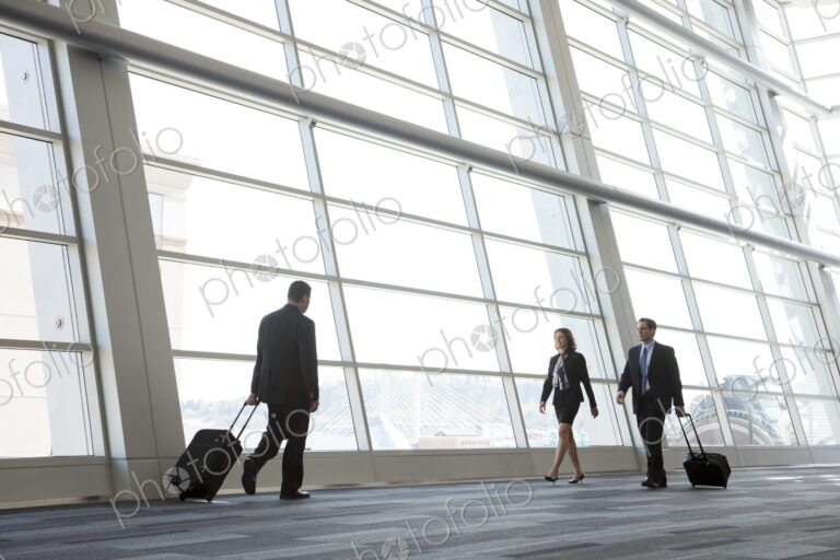 Three business people walking next to a large window in a conference centre lobby.