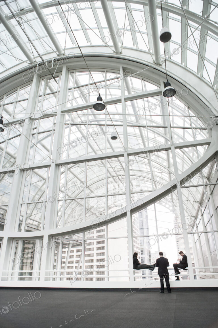 Three businesspeople meeting in front of a window in a large convention center loggy.