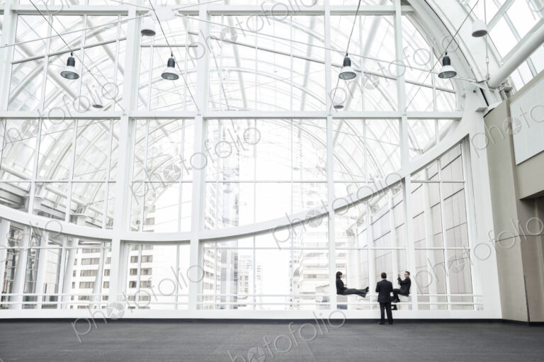 Three businesspeople meeting in front of a window in a large convention center loggy.
