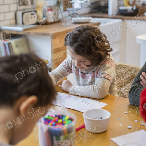 Three children and an adult woman at a table, drawing and writing cards and letters to…