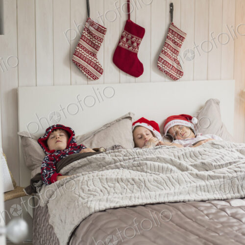 Three children in a double bed, with Christmas stockings hanging on the wall above… Three children in a double bed, with Christmas stockings hanging on the wall above…