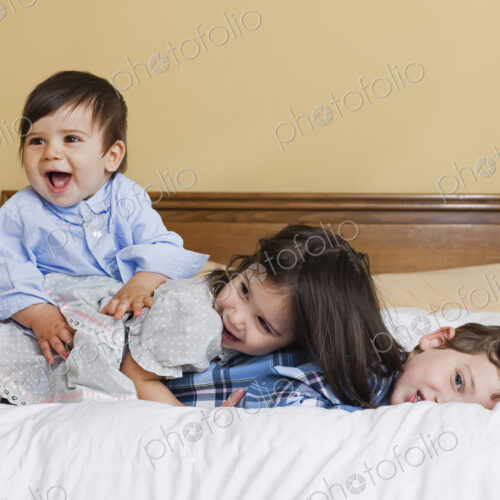 Three children in a family, lying playing on a large bed. Three children in a family, lying playing on a large bed.