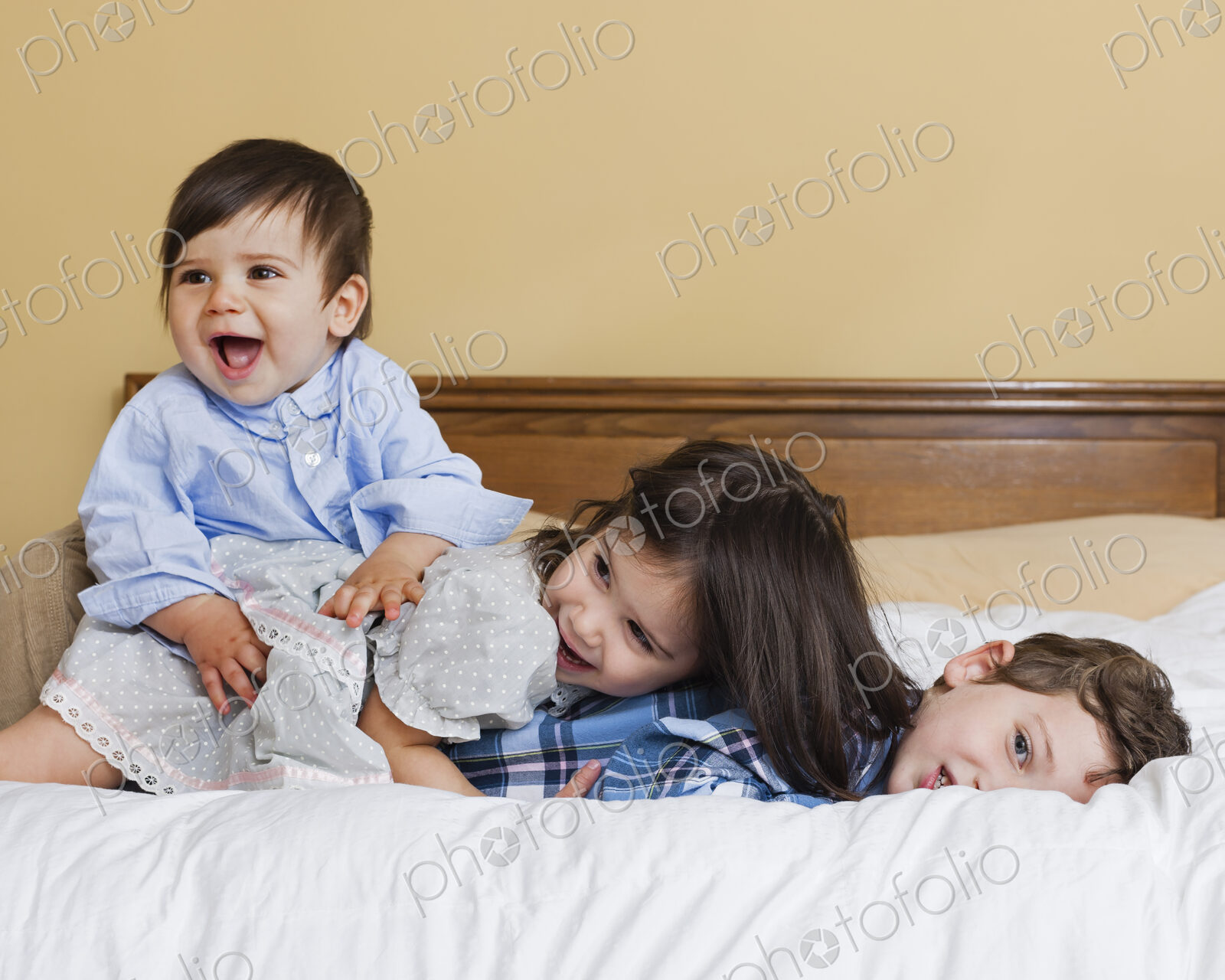 Three children in a family, lying playing on a large bed.