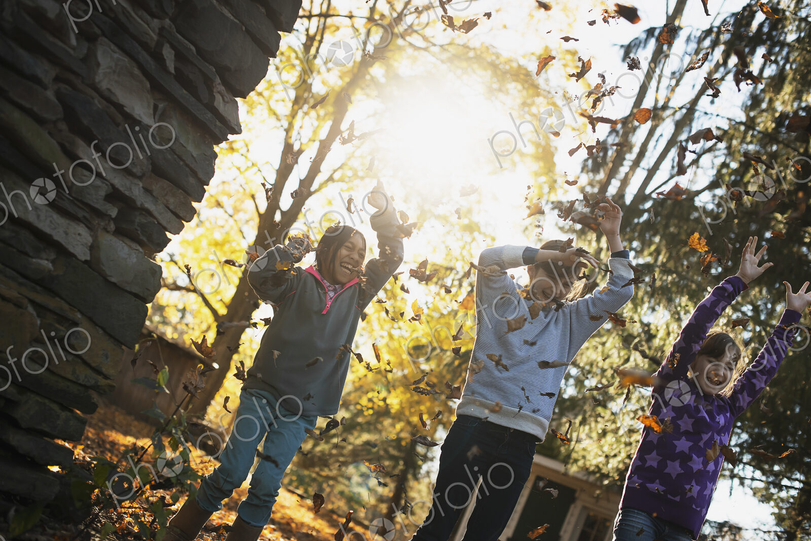 Three children in the autumn sunshine. Playing outdoors throwing the fallen leaves in…