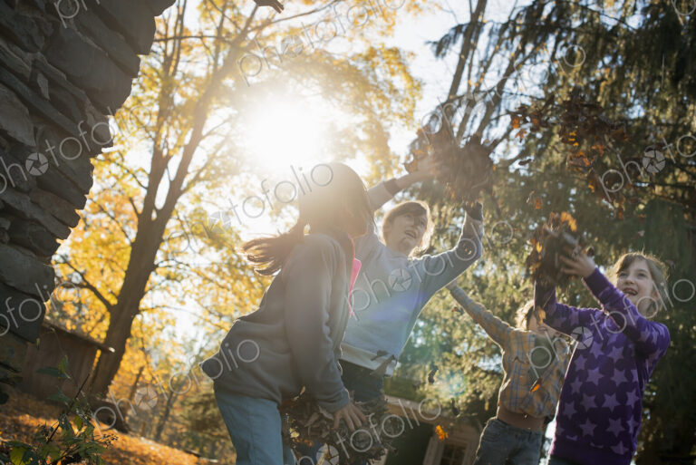 Three children in the autumn sunshine. Playing outdoors throwing the fallen leaves in…