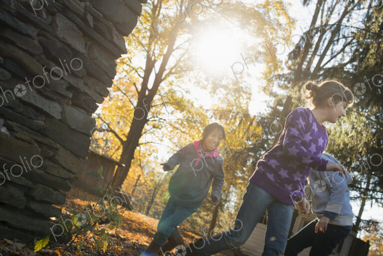 Three children in the autumn sunshine. Playing outdoors throwing the fallen leaves in…